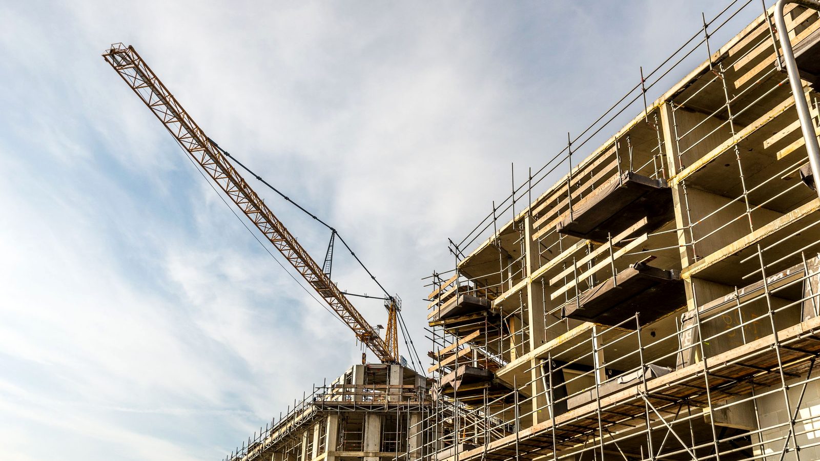 Public works construction site with a tower crane and scaffolding on a bonded project, where performance and payment bonds protect the public owner